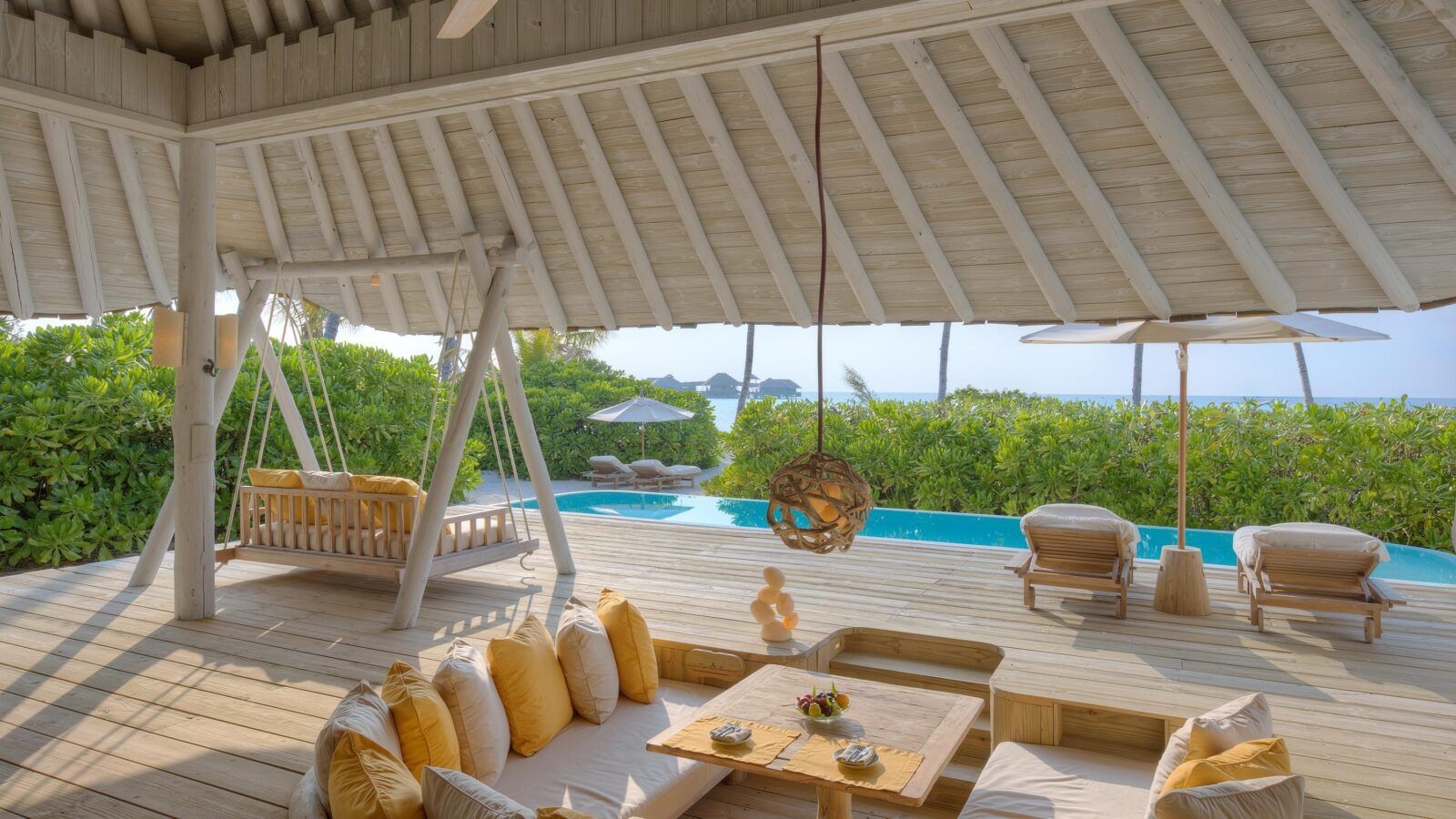 the image shows the outdoor space at beach hideaway villa at soneva secret with sofa a swing and swimming pool with ocean beach and view.
