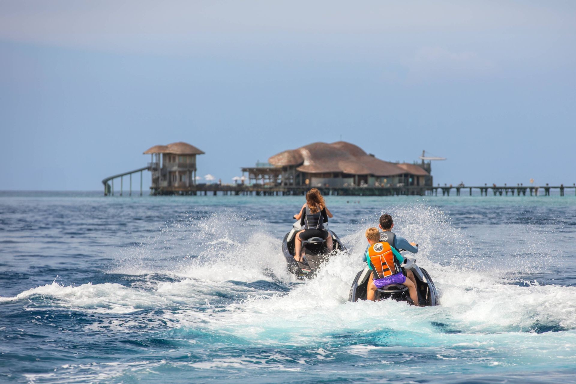Two individuals with kids riding jet skis on a sunny day, splashing through the water with excitement. 