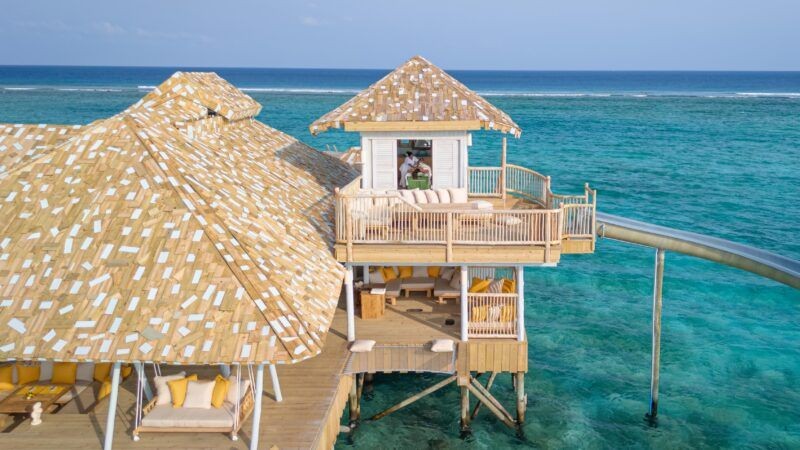  A seaside wooden house includes a slide that leads directly into the ocean, surrounded by scenic views.